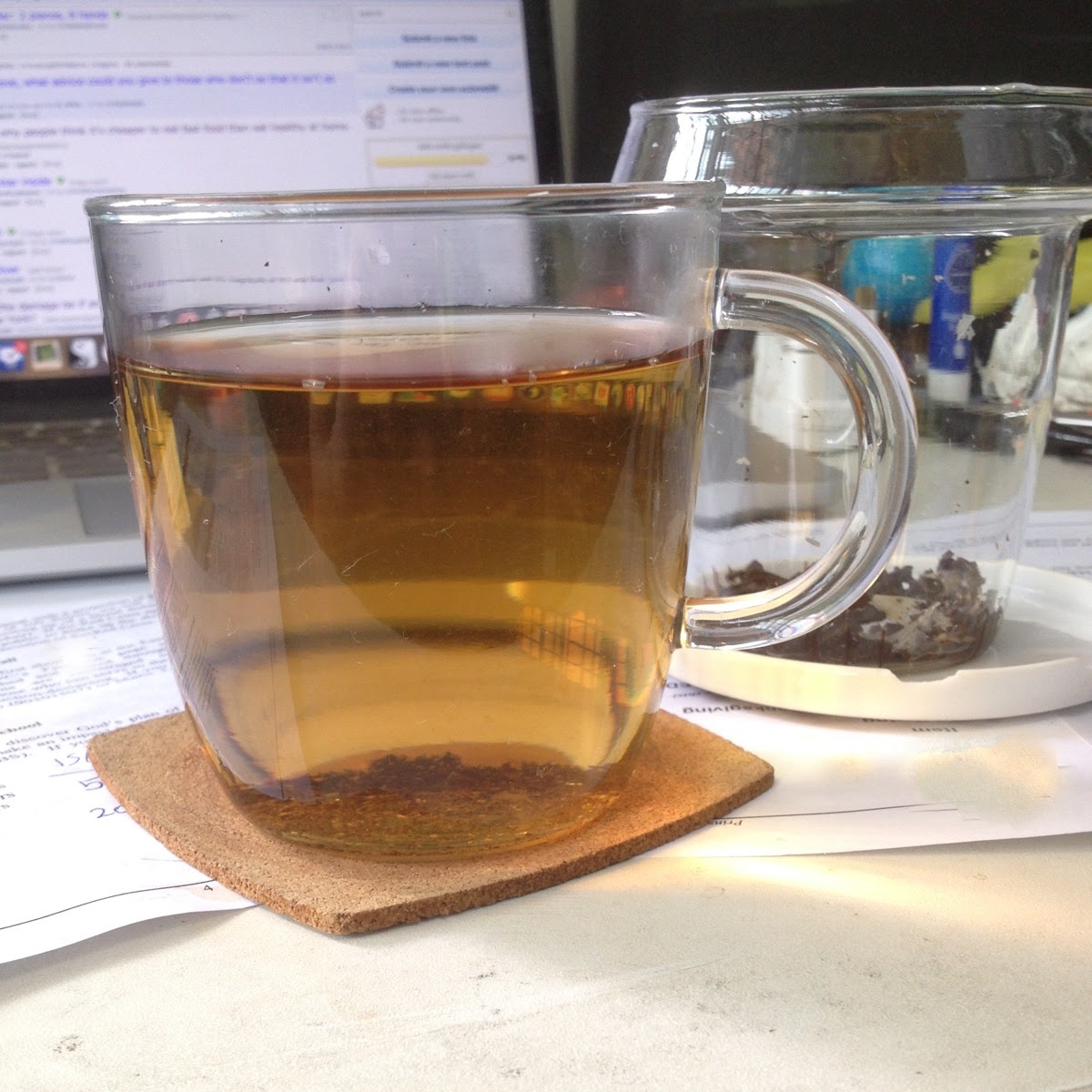 A glass cup of tea, with a matching glass tea infuser in the background