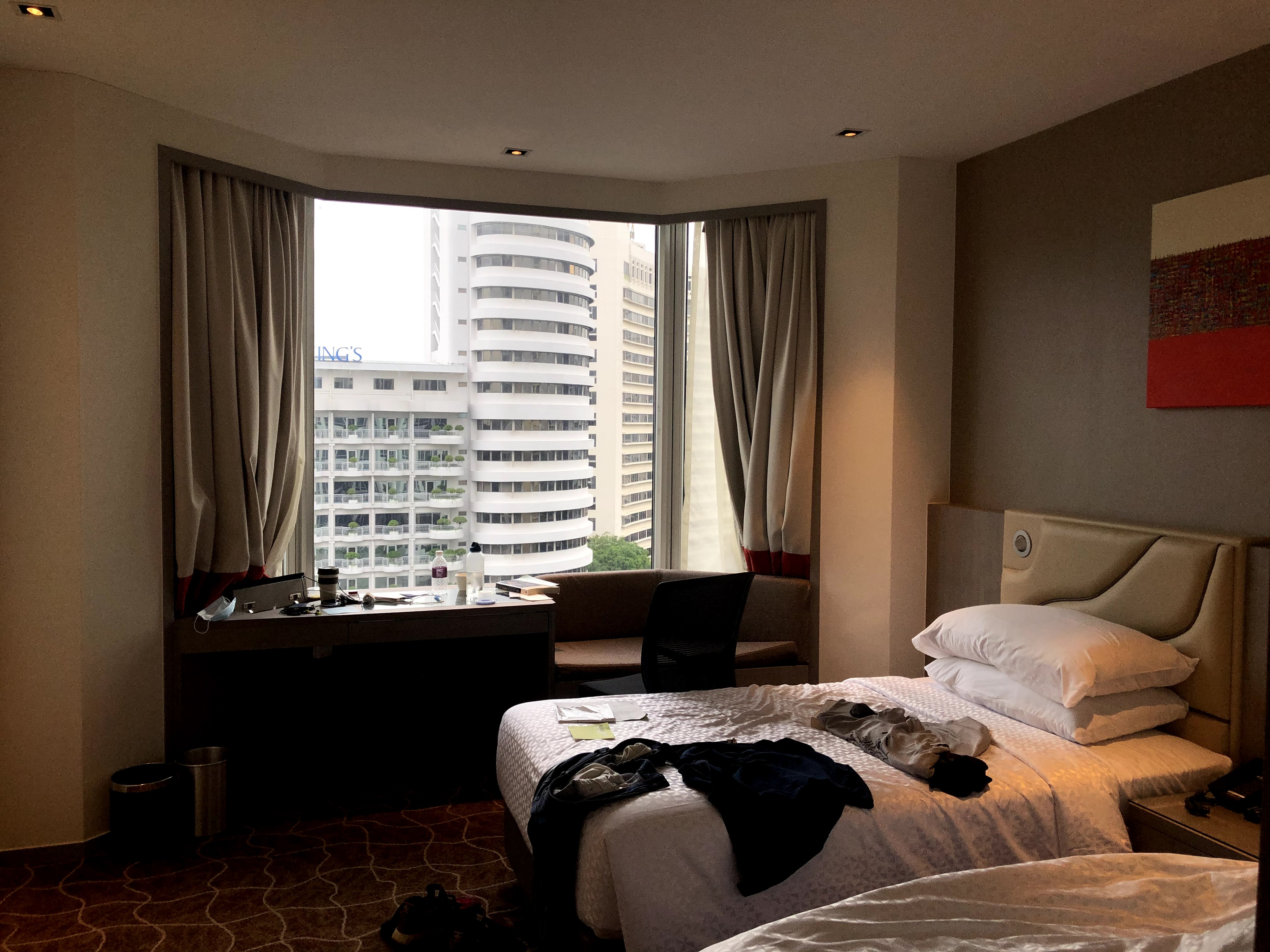 View of a hotel room with clothes spread out across one bed, with a view out the window of other hotels beyond