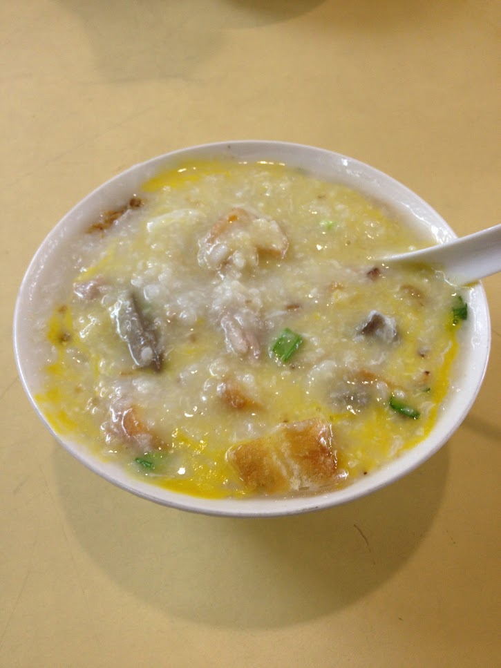 A bowl of pork congee in a white bowl, the congee yellow from having a raw egg yolk mixed into it